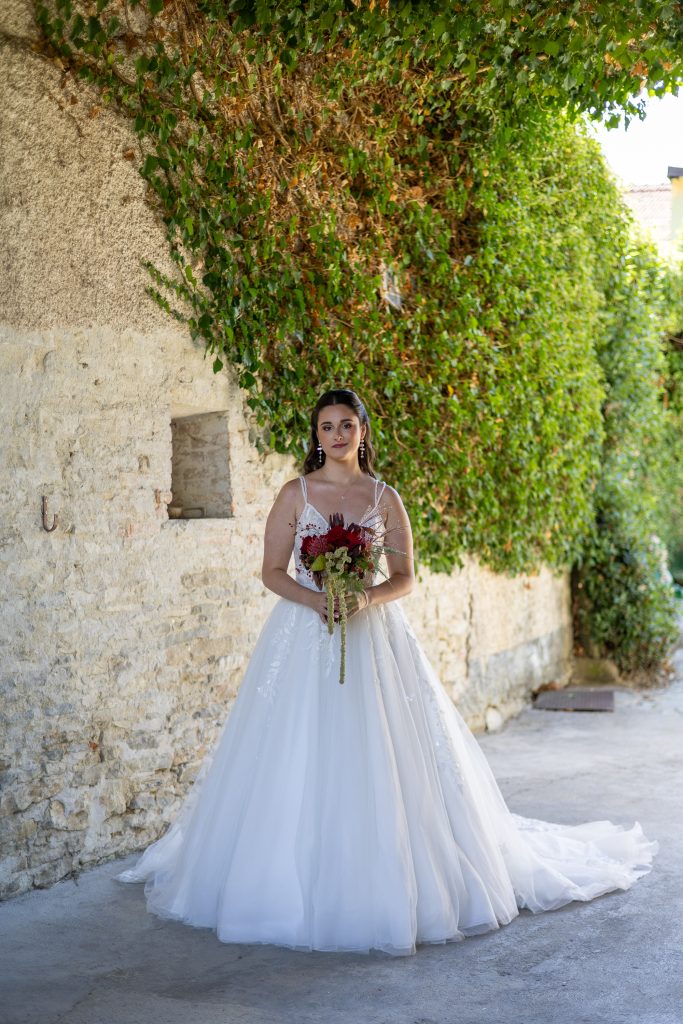Model in een witte trouwjurk met boeket op de binnenplaats in Italië